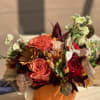 Orange pumpkin-shaped container with mixed autumn flowers and ribbon