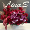 Red roses and purple orchids in a round gray vase with a ribbon