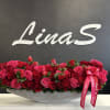 Long arrangement of red and pink roses in a gray container with a pink ribbon