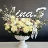 White rose arrangement in a white pedestal vase with a ribbon