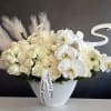 Cream roses and white orchids arranged in a textured white vase.