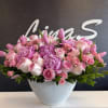 Low white bowl filled with dense pink peonies, roses, spray roses, and tulips