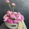 Pink peonies arranged in a white oval container with trailing cream flowers