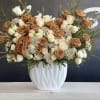Large rose arrangement in a white vase with tan and white blooms