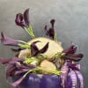 Purple calla lilies arranged in a purple bowl with wood slices and pinecones