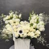 White floral arrangement in a tall square vase with roses and tulips