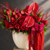 Red roses and anthuriums in a white vase with a burgundy ribbon
