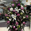 This dignified funeral arrangement features lavender roses, white lilies, and carnations, accented
