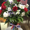 The "Liberty Blooms" arrangement features a vibrant mix of red roses, carnations