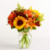Bouquet of sunflowers, orange roses, and lilies in a clear glass vase