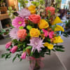 Mixed bouquet of roses, gerbera daisies, chrysanthemums, and calla lilies in a glass vase
