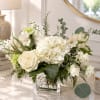 White floral arrangement in a clear glass vase with roses and hydrangeas