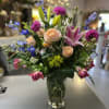 Mixed bouquet with roses, lilies, and blue flowers in a glass vase