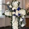 White floral cross arrangement with blue accents on an easel