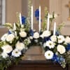 White roses and daisies arranged with blue flowers and tall white candles
