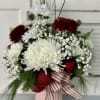 Red and white floral arrangement in a striped ribbon-wrapped container