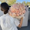Woman holding a bouquet of pale pink roses wrapped in beige paper
