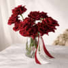 Red roses in a clear glass vase with red and white ribbons