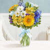Mixed bouquet of daisies, gerberas, and blue flowers in a glass vase