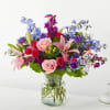 Mixed bouquet of pink, purple, and blue flowers in a glass vase