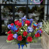 Red roses and blue flowers in a white vase with a ribbon