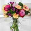 Mixed bouquet of roses, carnations, and gerbera daisies in a clear glass vase