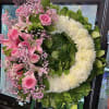 Pink lilies and roses arranged in a heart-shaped wreath with white flowers.