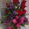 Red roses and purple flowers in a tall glass vase with a pink ribbon