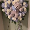 Heart-shaped floral wreath with a teddy bear and blue ribbon on an easel