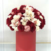 Round arrangement of red, pink, and white roses with orchids in a tall red hatbox-style container