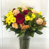 Mixed bouquet of yellow daisies, peach roses, and burgundy gerberas in a glass vase