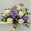 White roses and purple flowers arranged in a white vase