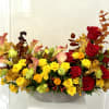 Autumn floral arrangement with red roses, yellow blooms, and calla lilies in a low bowl