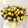 Rounded arrangement of yellow roses with purple filler flowers in a cream ceramic pot