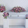 Funeral casket surrounded by pink and purple floral sprays