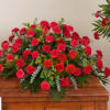 Large red carnation arrangement with greenery on a wooden casket