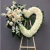 Heart-shaped white floral wreath on an easel with a small bouquet of pale roses