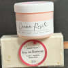A pink cream jar sits on top of a wrapped facial soap bar.