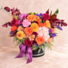 Mixed bouquet of roses, chrysanthemums, and hydrangeas in a black hat box with purple ribbon