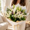 Bouquet of white lilies and cream roses wrapped in white paper with gold trim
