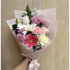 Handheld bouquet of pink, white, and red mixed flowers wrapped in pale pink paper
