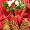 Red and white floral arrangement in a metallic vase with pinecones