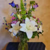 Mixed bouquet of white lilies, purple blooms, and pink roses in a glass vase