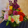 Mixed bouquet in a dark vase with roses, lilies, hydrangea, and bright accent flowers
