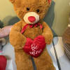 Brown teddy bear holding a red heart pillow with a ribbon