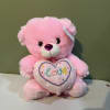 Pink teddy bear holding a heart with the word love