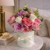 Pink and white roses arranged in a round white box with a ribbon