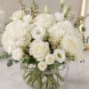 Rounded bowl of white roses, hydrangeas, and lisianthus in a clear glass