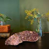 Amethyst crystal cluster on a dark surface with a glass vase and plant stems