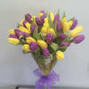Bouquet of yellow and purple tulips in a clear glass vase with a purple ribbon